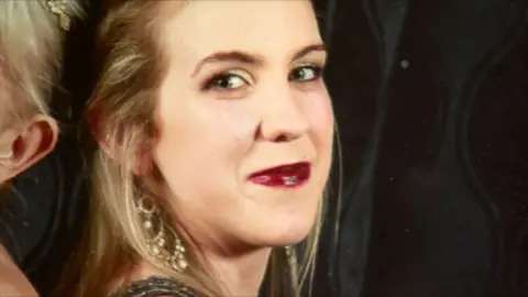 A woman looking at the camera, she has light hair and is smiling.