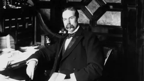 Getty Images An old black and white photograph, showing Thomas Lipton - a man in a suit, with bow tie and with a bushy moustache, sitting at a desk
