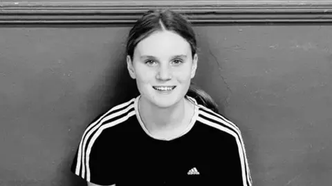 Family handout Black and white photo of Holly Newton. She is wearing an adidas t-shirt and her hair is tied back. She is smiling and looking directly at the camera.