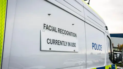 Merseyside Police The side of a white police van with a sign reading 'Facial Recognition Currently in Use' 