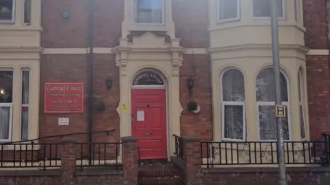 Google A red brick terraced building with a red door and a red sign for Gabriel Court Care Home.