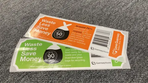 BBC Two rectangular bin stickers laying on a grey carpet. The bottom sticker is a lime green colour and the top sticker is orange. 