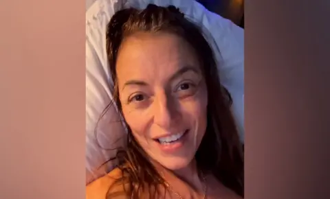@davinamccall / Instagram A close up selfie of Davina McCall looking at the camera while lying in a hospital bed, she's smiling as she's talking into camera.