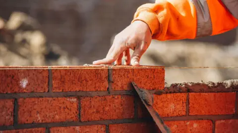 Getty Images A hand placing a brick on a partially built wall