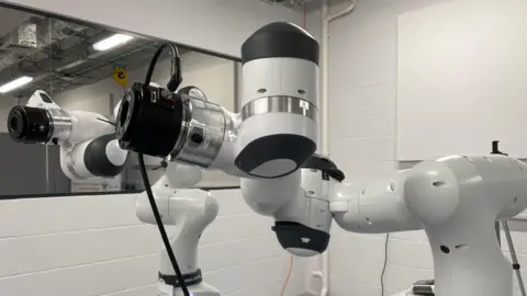 BBC/JULIA LEWIS Two white and black robotic arms in a laboratory setting
