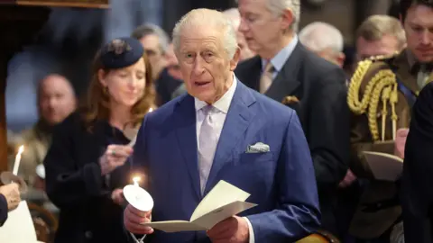 PA Media The King holds a lit candle and service booklet as he attends an Advent Service at Westminster Abbey