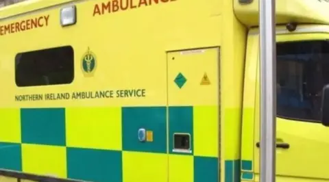 The side of an ambulance - blue and green checked design - which says NI ambulance service on the side, along with it crest.