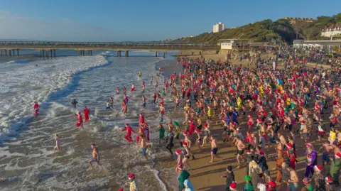 A picture taken from a drone showing hundreds of people, many dressed in fancy dress, running into the sea.