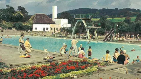 Museum in the Park, Stroud A old colour photo of Stroud Lido as it was in the 1940s, with beautiful flower beds in the foreground and rolling hills in the background. 