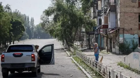 Getty Images Ukrainian police officer, convinces a local resident, who refuses to be evacuated, to change her mind and leave Toretsk