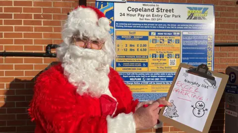 Father Christmas holding a naughty list that says "Excel Parking"