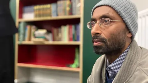 Jon Wright/BBC A close-up of Mojlum Khan's profile, who is wearing glasses and a woolly hat, and sits inside a mosque.