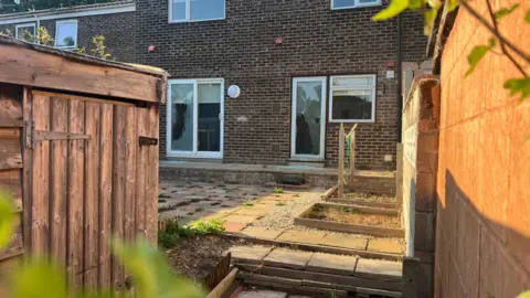 John Fairhall/BBC The rear of a brick-built house shows shattered glass panes on a patio and door.