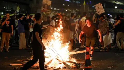 Reuters Protesters rally against the government around a fire and holding placards, to show support for the hostages who were kidnapped during the deadly October 7 attack.