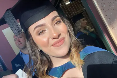 Sophie Morgan Sophie Morgan wears a black university cap and gown and smiles at the camera. She has brown short hair and brown eyes. 