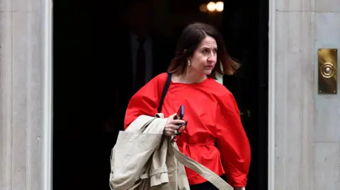 Liz Kendall leaving Downing Street wearing a red top avd carrying a beige coat