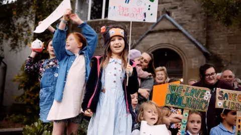 Children holding signs reading 'save our library'