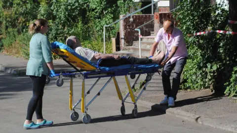 As pessoas da EPA/Shutterstock movem um homem em uma maca perto de um prédio residencial danificado depois de ser atingido em um golpe de drone em Odesa, Ucrânia