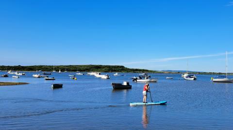 SUNDAY - A paddleboarder in Christchurch Harbour with boats in the water behind.