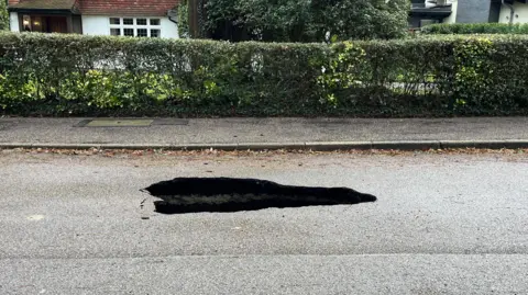 Nicola Hasler/BBC A large hole on the surface of a road outside a large house