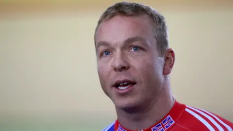 Reuters Sir Chris Hoy spogląda znad kamery. Ma krótkie, ciemnoblond włosy i niebieskie oczy i nosi czerwono-niebieską kurtkę z flagą Wielkiej Brytanii po obu stronach kołnierza.