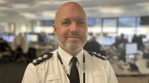 Chief Inspector, Al Lumley, in police uniform standing in the middle of the control room at Wiltshire Police Headquarters in Devizes