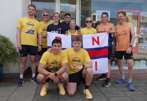 Helen Cowan The brothers crouch down in front of 8 members of the RNLI crew holding a banner. They are all wearing running gear.