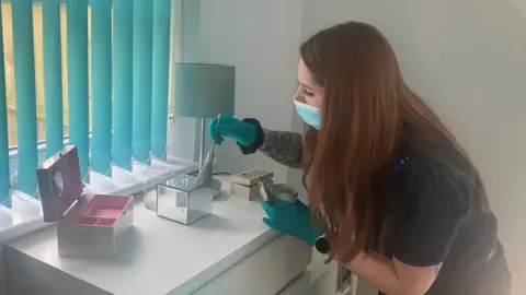 Photograph of a Hayley Craig, who works as a CSI at Greater Manchester Police. She's using a brush to look for fingerprints on a jewellery box. 