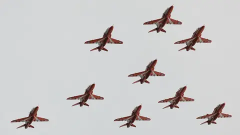 The Red Arrows flying in formation, with a grey sky above them.
