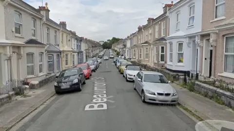 Google The image shows a residential street named Beaumont Street, lined with terraced houses on both sides. Several cars are parked along the street, and the houses share similar architectural styles with minor differences in colour and design.