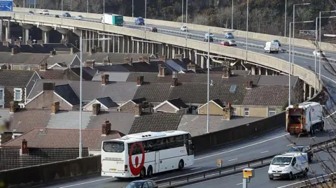 Getty Images Cars, a bus, a dustbin lorry and vans on the M4 motorway flyover at Port Talbot as it passes by terraced houses