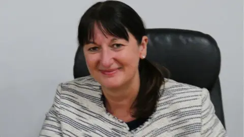 Caerphilly Council A picture of Christina Harrhy sat on a black chair in front of a white wall.