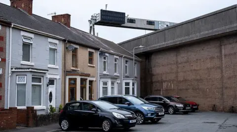 Getty Images Cars parked outside houses in a cul-de-sac street in front of a large concrete wall which holds up the M4 motorway at Port Talbot