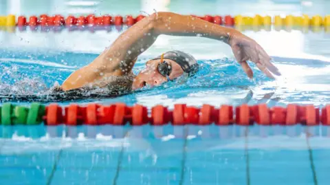 A lone female swimmer in a black hat and goggles doing the front crawl