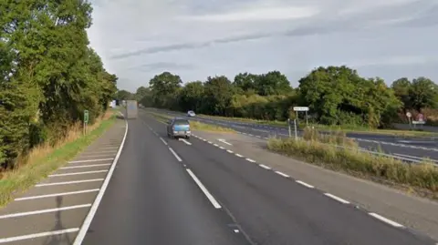 The A1 road going southbound with the northbound carriage on the right side. It is lined by trees on both sides and there is a junction off to the right. There is a sign saying "Water Newton" on the right.