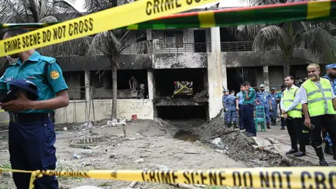 Getty Images Yellow police tape saying 'Police line do not cross' in front of a burnt building and a group of emergency workers