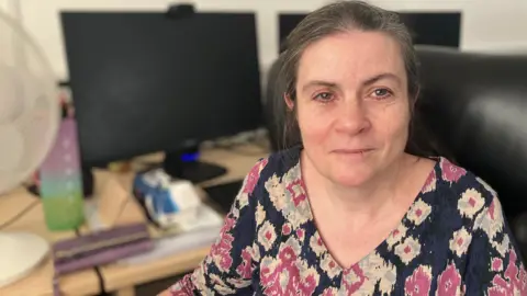 Louise, a woman, wearing a pink and white printed navy shirt, smiling for camera.