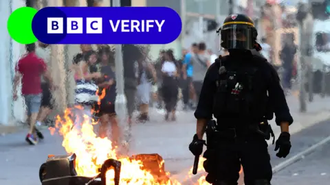 A French riot police officer stands guard next to a burnt out trash bin during a demonstration against police in Marseille, southern France on July 1, 2023