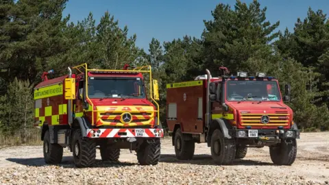 DWFRS The new and old Unimog vehicles parked side by side. It is a sunny day.