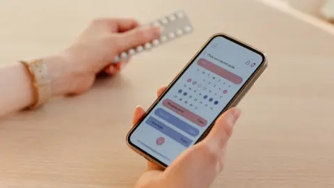 Getty Images Woman holding her phone with a cycle tracking app open