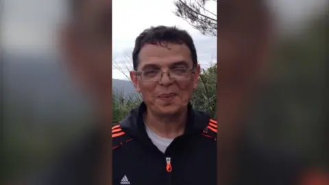 Leia Roitour Boris Tetleroyd wearing glasses and dressed in a black shirt with bright orange stripes on the shoulders.