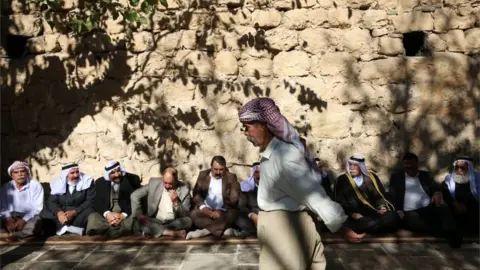 EPA Men sit against a wall in Lalish ahead of the inauguration ceremony for the new Yazidi spiritual leader