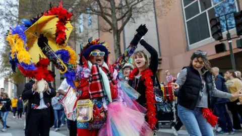 Three people wearing red boas dance in New Orleans ahead of the Sugar Bowl