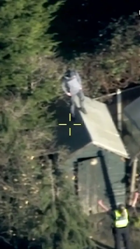 A man in a grey tracksuit stood on top of a green garden shed