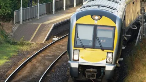 Getty Images A Translink train in green, silver and yellow livery, travels along a track towards the camera