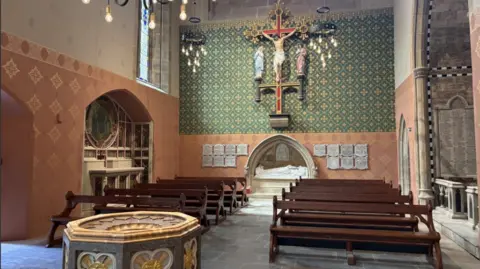 Interior of smaller area within the cathedral with dark wooden pews, salmon and green walls.