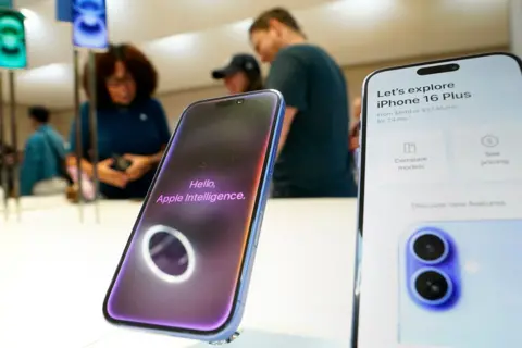 AFP via Getty Images An iPhone 16 with the words 'hello, Apple Intelligence' sits next to another iPhone with the words 'let's explore iPhone 16 Plus' while on display with customers browsing in the background, in a US Apple store in 2024.