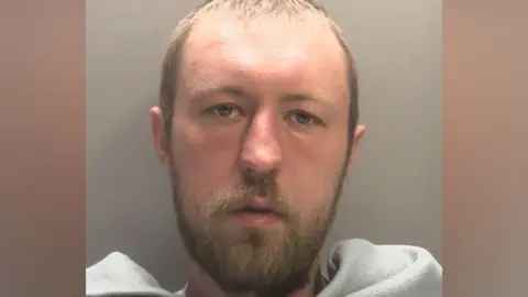 West Midlands Police A mug shot of John Ashby who has short light brown hair and facial hair. he has a grey blanket across his front