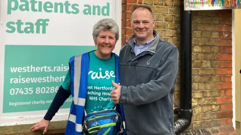 Justin Dealey/BBC Linda Pottinger smiling with surgeon Drostan Cheetham who has a thumbs up