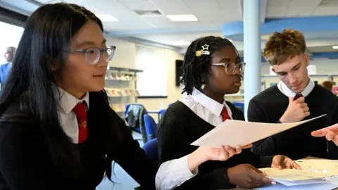 Three young people sitting at a table in school having just received their 2026 Scottish qualifications
